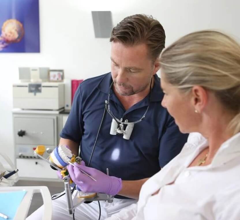 Zahnarzt Dr. Gottschlich demonstriert einer Patientin die Behandlung an einem Zahn Modell aus Gips